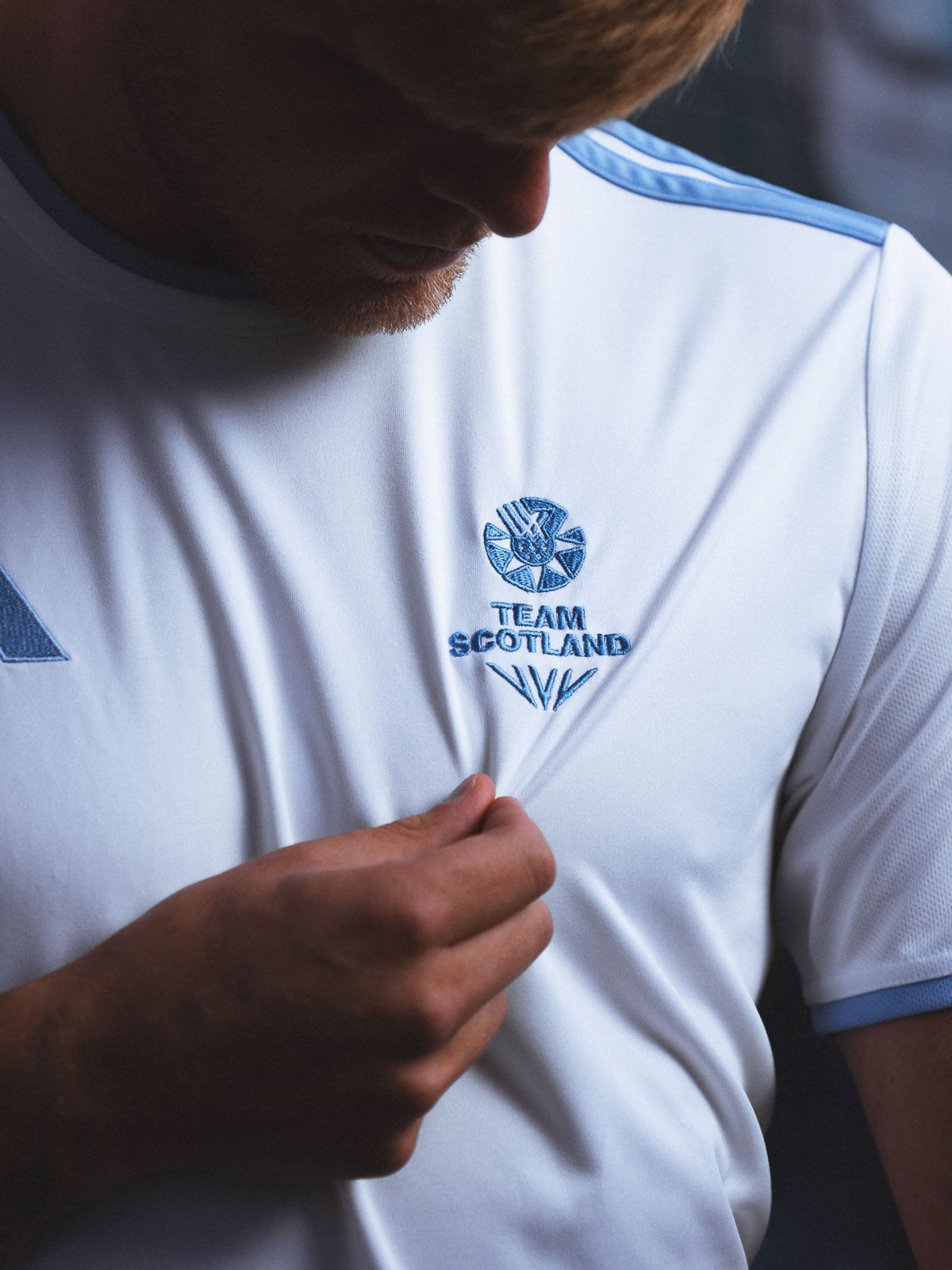 Close up view of man wearing white adidas Team Scotland jersey showing Team Scotland logo embroidery.