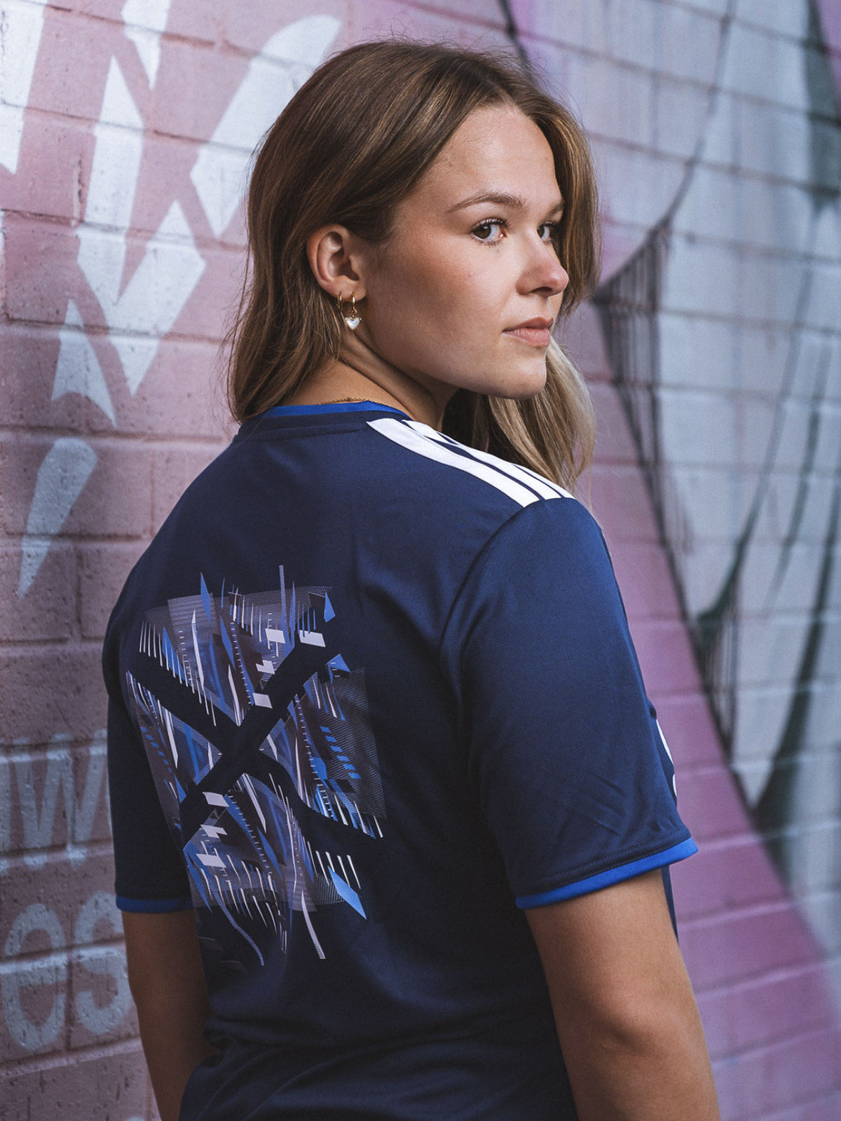 Three quarter view of woman wearing navy adidas Team Scotland Jersey showing saltire back print.