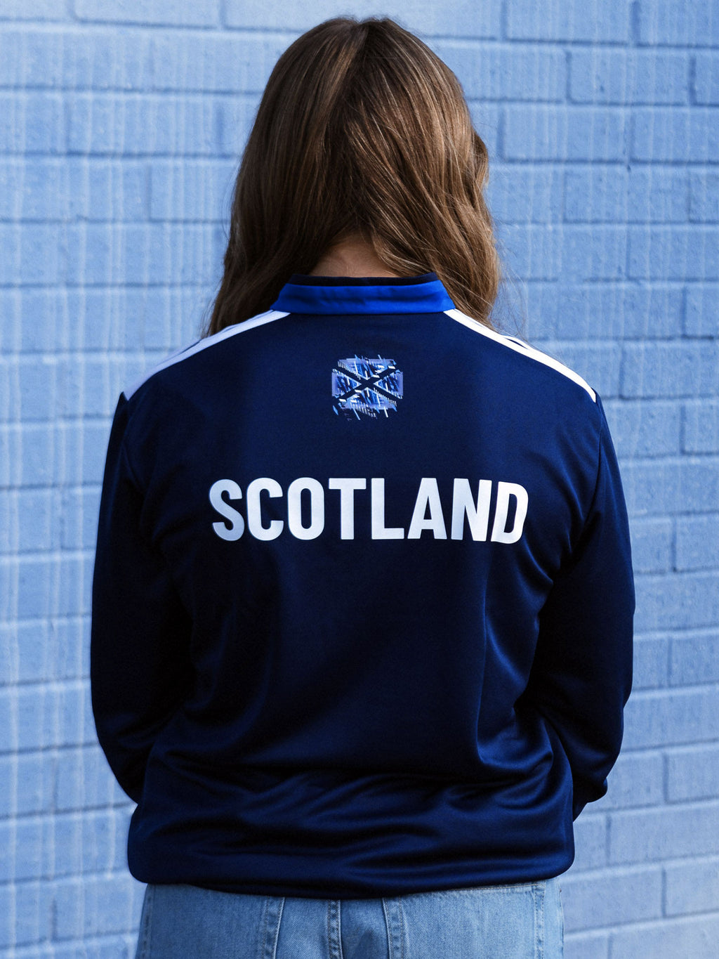 Back view of woman wearing navy three quarter zip adidas Team Scotland track top.